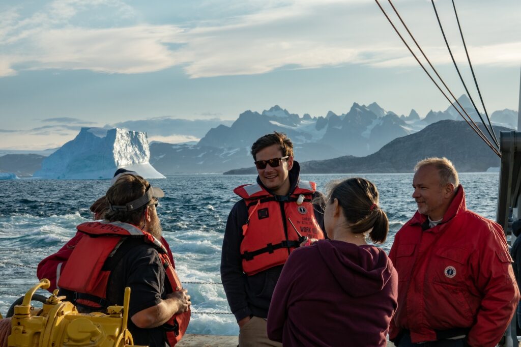 Foukal (center) smiling with a group of researchers on a boat off the southern coast of Greenland.