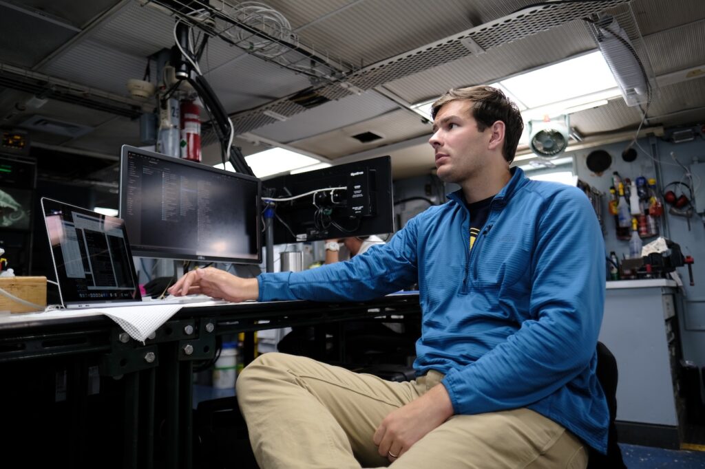 Foukal sits at a computer screen inside of a research vessel. 