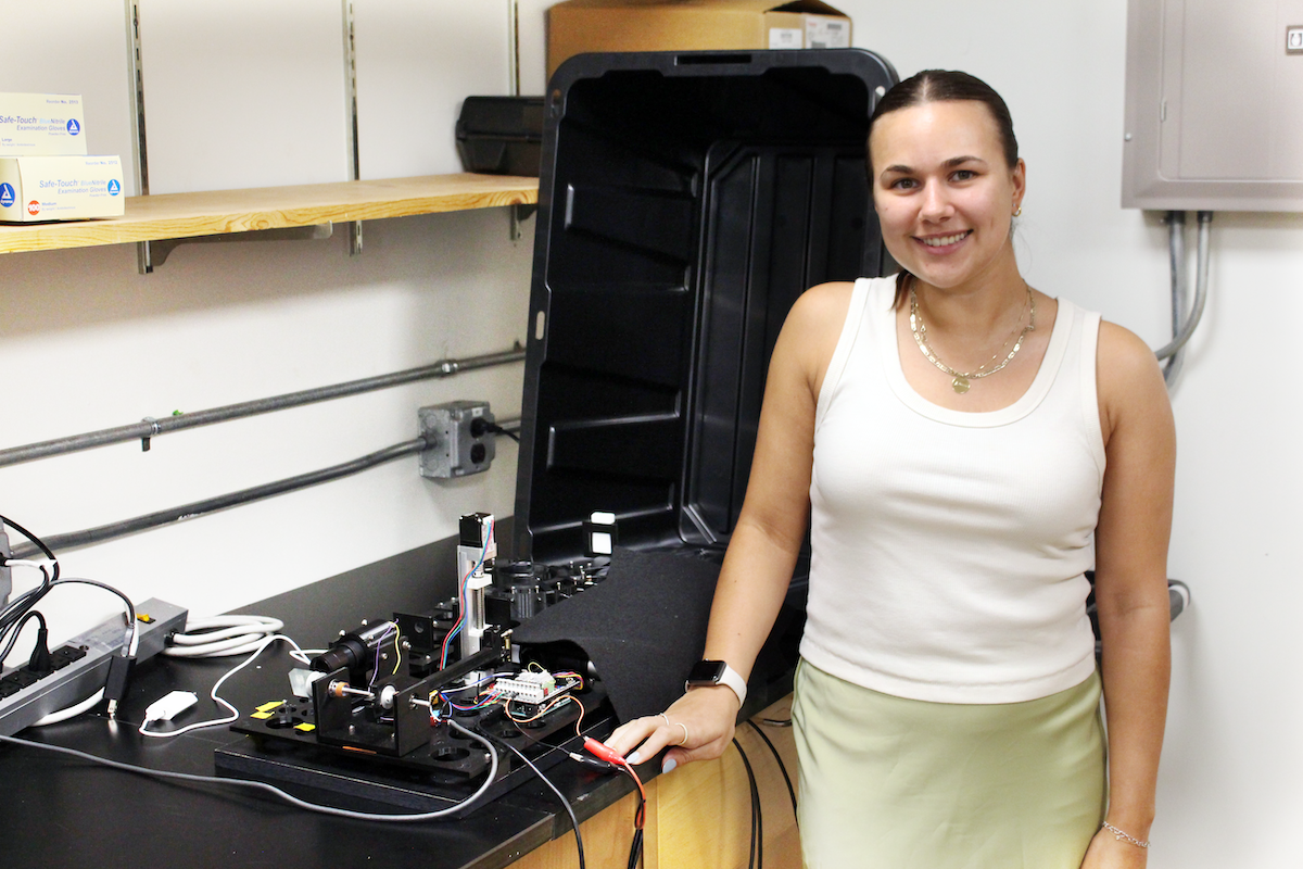 Ashley Ohall stands in front of her instrument sitting on a lab bench.